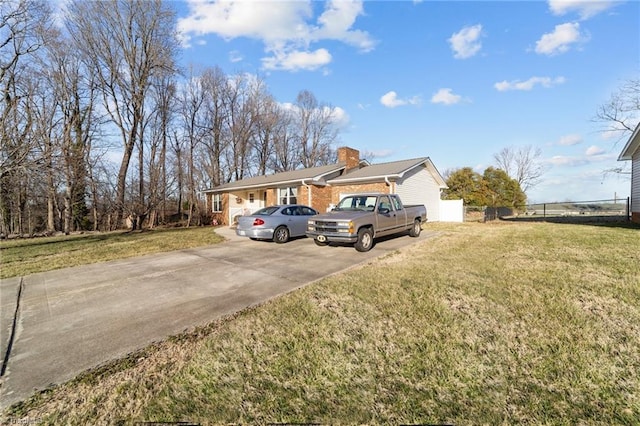 view of front facade featuring concrete driveway, a chimney, a front yard, and fence