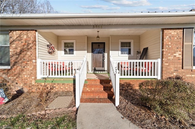 view of exterior entry with a porch and brick siding