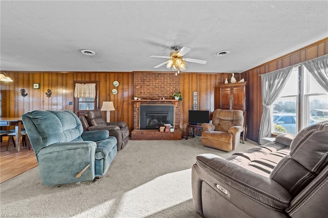 carpeted living area featuring a textured ceiling, a fireplace, a ceiling fan, and wooden walls