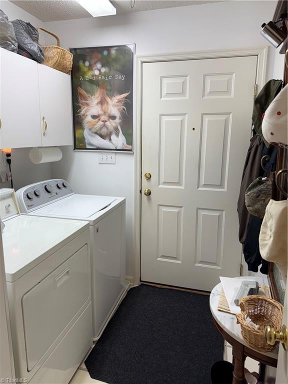 laundry area with cabinets, washing machine and clothes dryer, and a textured ceiling