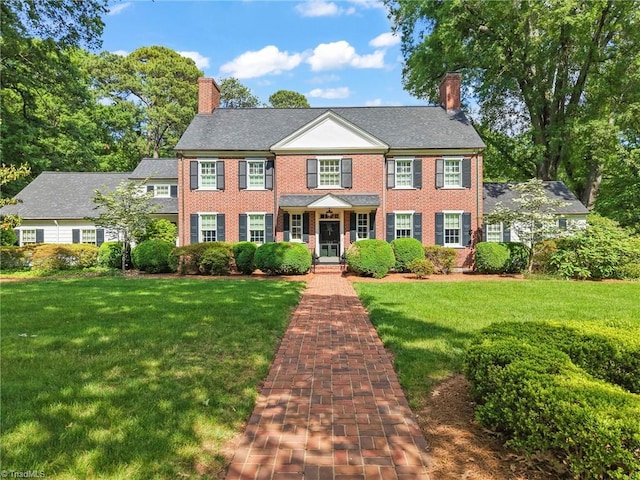 colonial house with a chimney, a front yard, and brick siding