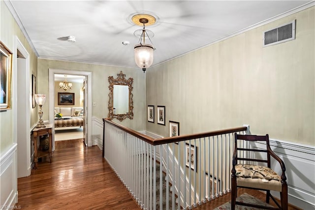 hallway with wood finished floors, a chandelier, crown molding, and an upstairs landing