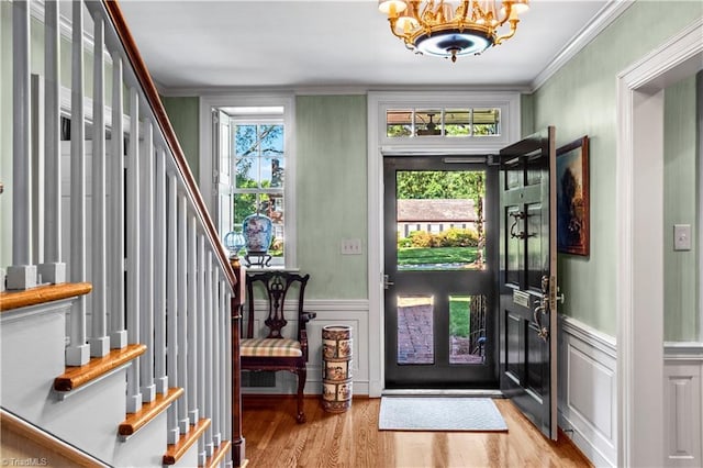 foyer featuring a chandelier, stairway, light wood finished floors, ornamental molding, and wainscoting