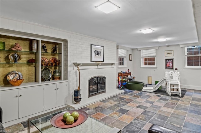 living area with stone finish flooring, a fireplace, baseboards, and crown molding
