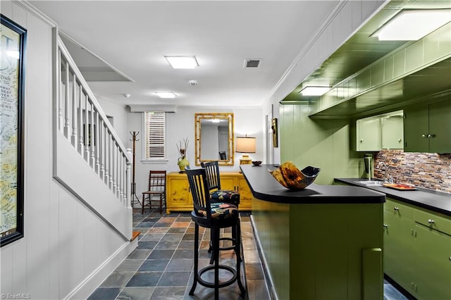 kitchen with green cabinets, dark countertops, dark stone finish flooring, tasteful backsplash, and a breakfast bar area