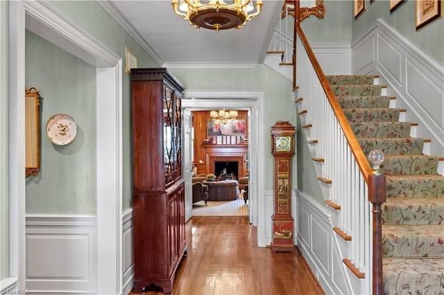 stairway with a chandelier, a decorative wall, wood finished floors, ornamental molding, and a wainscoted wall