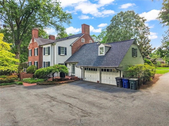 view of front facade with a garage, asphalt driveway, roof with shingles, and a chimney
