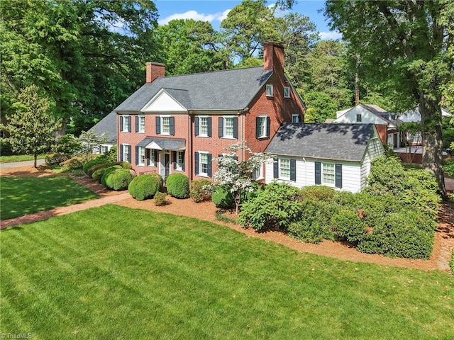 colonial home featuring a chimney, a front yard, and brick siding