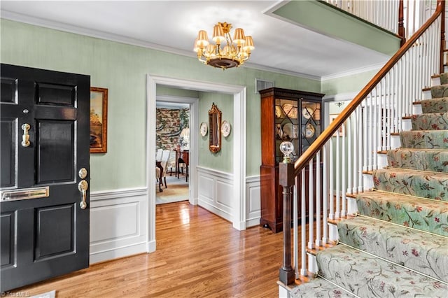 foyer entrance with a chandelier, stairs, light wood finished floors, crown molding, and wainscoting