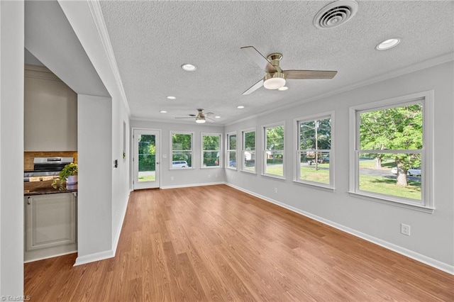 unfurnished sunroom with crown molding, a textured ceiling, visible vents, and a healthy amount of sunlight