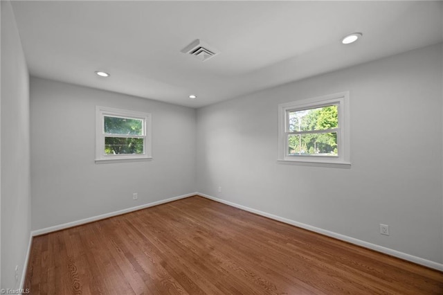 empty room featuring visible vents, wood finished floors, baseboards, and a healthy amount of sunlight