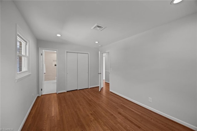 unfurnished bedroom with a closet, wood finished floors, recessed lighting, connected bathroom, and baseboards