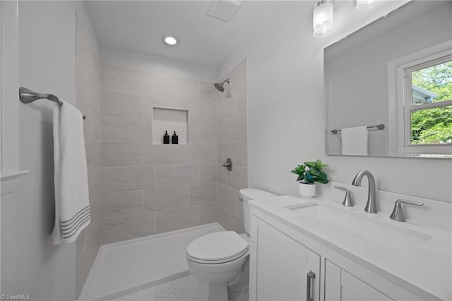 full bathroom featuring toilet, a tile shower, vanity, and visible vents