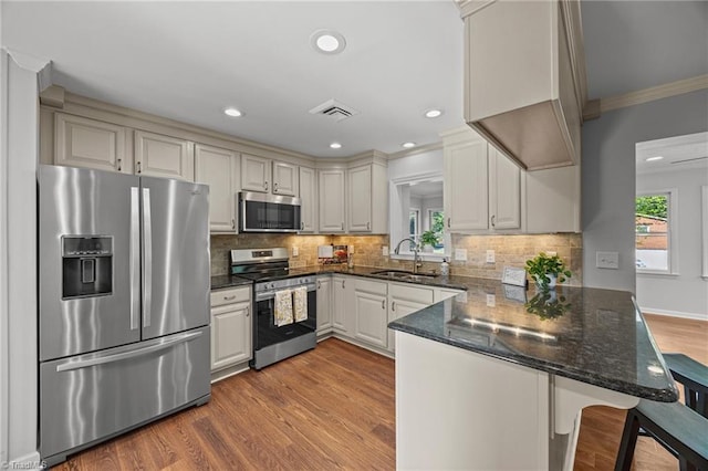 kitchen featuring a sink, a peninsula, wood finished floors, ornamental molding, and appliances with stainless steel finishes