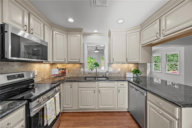kitchen featuring light wood-style flooring, a sink, a peninsula, decorative backsplash, and appliances with stainless steel finishes