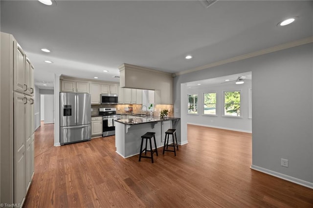 kitchen featuring a peninsula, a breakfast bar area, a sink, stainless steel appliances, and ornamental molding