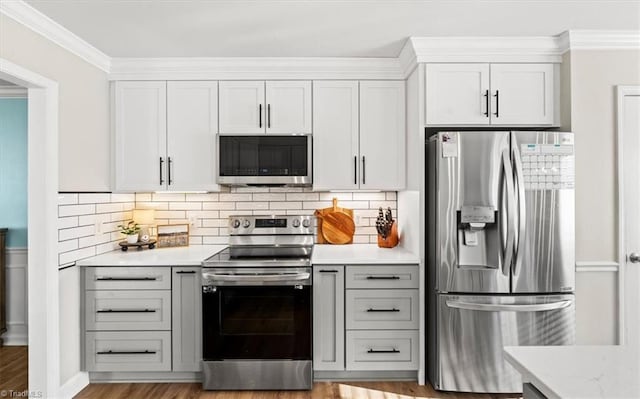 kitchen with backsplash, appliances with stainless steel finishes, white cabinets, and light hardwood / wood-style floors