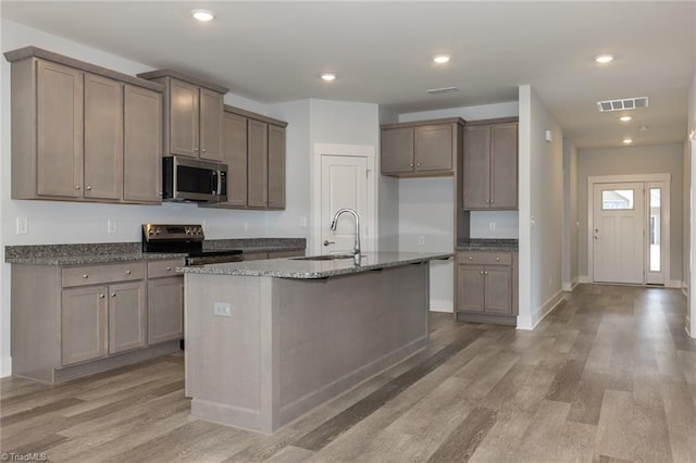 206 Cason Dr, Gibsonville, NC 27249 - kitchen featuring stainless steel appliances, light wood-style flooring, a sink, dark stone counters, and an island with sink