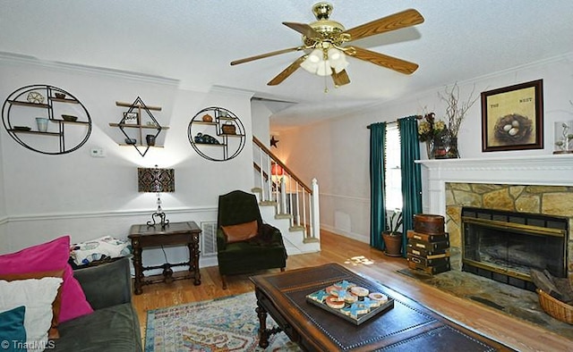 living room featuring ceiling fan, wood-type flooring, ornamental molding, and a fireplace