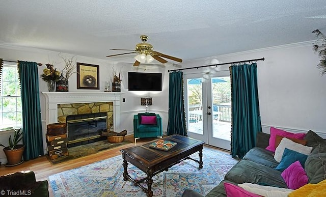 living room featuring ceiling fan, a textured ceiling, ornamental molding, a fireplace, and light hardwood / wood-style floors