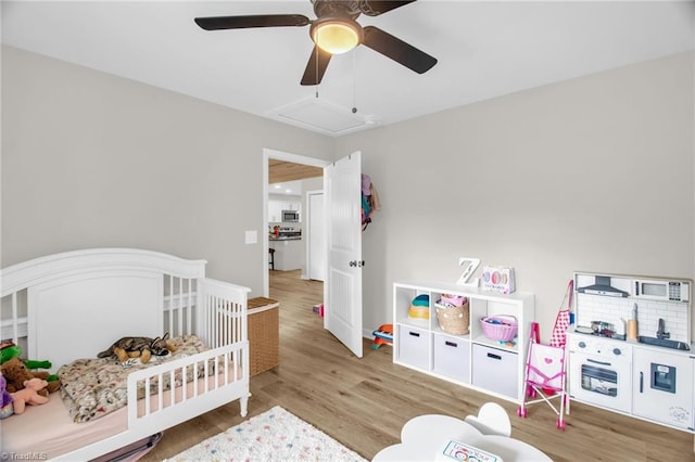 bedroom featuring a crib, a ceiling fan, and wood finished floors