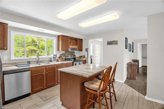 kitchen with a sink, a kitchen breakfast bar, brown cabinets, and stainless steel appliances