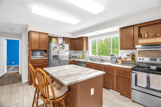 kitchen featuring a kitchen island, a kitchen breakfast bar, under cabinet range hood, a sink, and appliances with stainless steel finishes