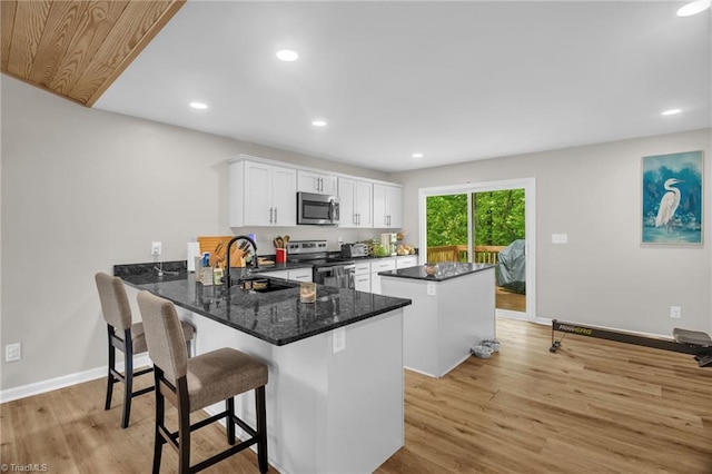 kitchen with light wood-style floors, a center island, white cabinets, a sink, and appliances with stainless steel finishes
