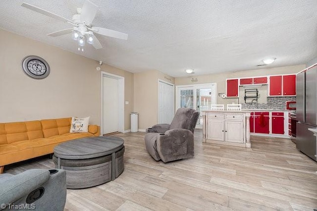 living room with ceiling fan, sink, light wood-type flooring, and a textured ceiling