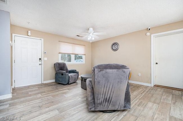 living area with a textured ceiling, light hardwood / wood-style flooring, and ceiling fan