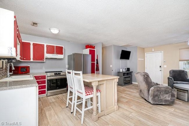 kitchen with a textured ceiling, stainless steel appliances, sink, a center island, and light hardwood / wood-style floors