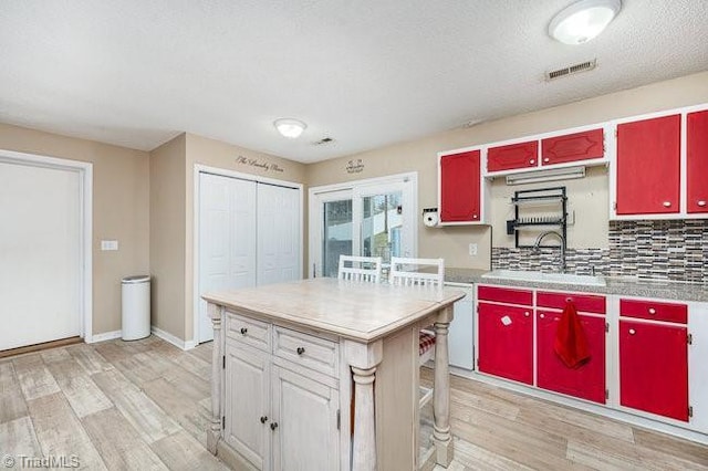 kitchen featuring dishwasher, backsplash, sink, light wood-type flooring, and a kitchen island