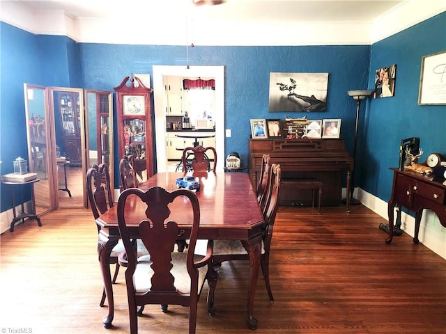 dining area featuring wood finished floors, a textured wall, and ornamental molding