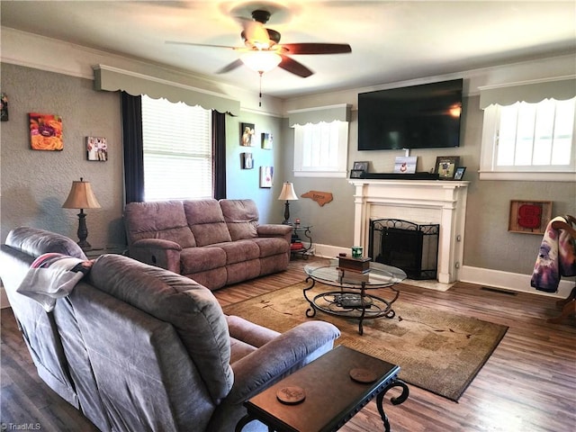 living area featuring ceiling fan, a fireplace with flush hearth, wood finished floors, and baseboards
