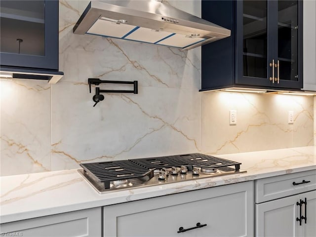 kitchen featuring light stone counters, backsplash, stainless steel gas cooktop, and exhaust hood