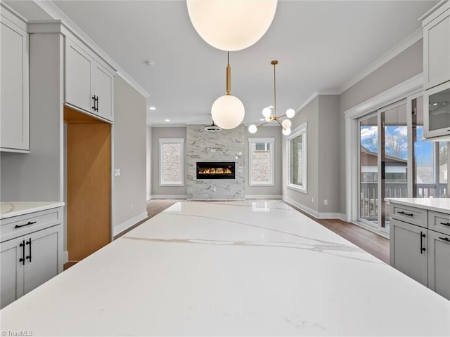 kitchen featuring crown molding, a high end fireplace, light stone countertops, and hanging light fixtures