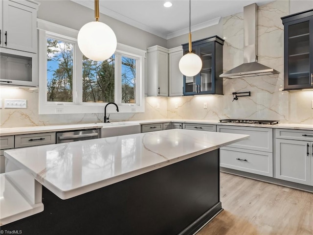 kitchen with sink, light hardwood / wood-style flooring, hanging light fixtures, stainless steel appliances, and wall chimney range hood