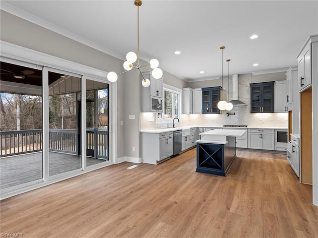 kitchen with crown molding, appliances with stainless steel finishes, a center island, decorative light fixtures, and wall chimney exhaust hood