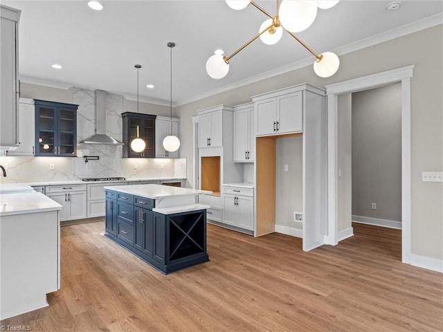 kitchen featuring wall chimney exhaust hood, a center island, ornamental molding, pendant lighting, and white cabinets