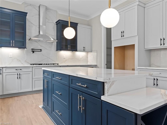 kitchen with blue cabinets, wall chimney range hood, white cabinets, and decorative light fixtures