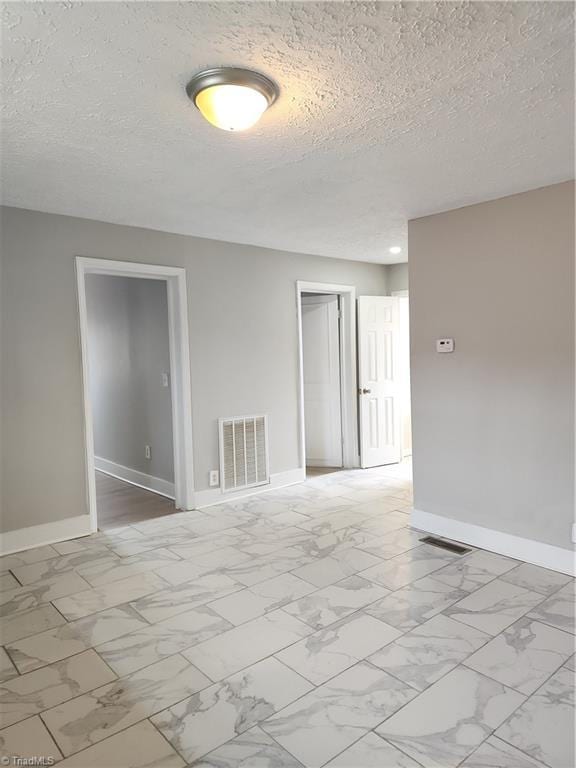 empty room featuring marble finish floor, baseboards, visible vents, and a textured ceiling