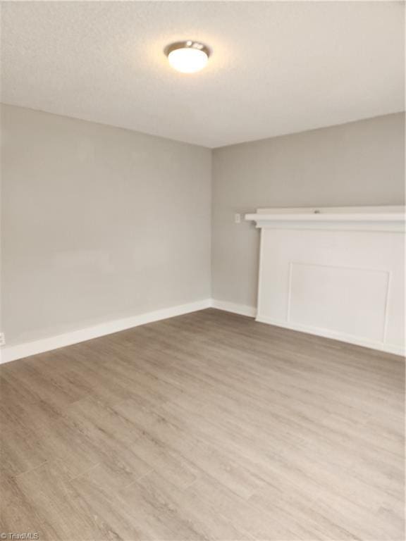 unfurnished living room with a textured ceiling, light wood-style flooring, and baseboards