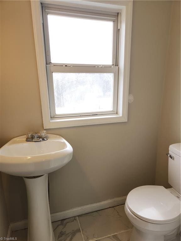 half bathroom featuring toilet, a healthy amount of sunlight, baseboards, and marble finish floor