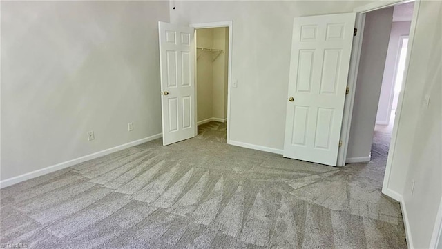 unfurnished bedroom featuring a closet, a spacious closet, carpet, and baseboards