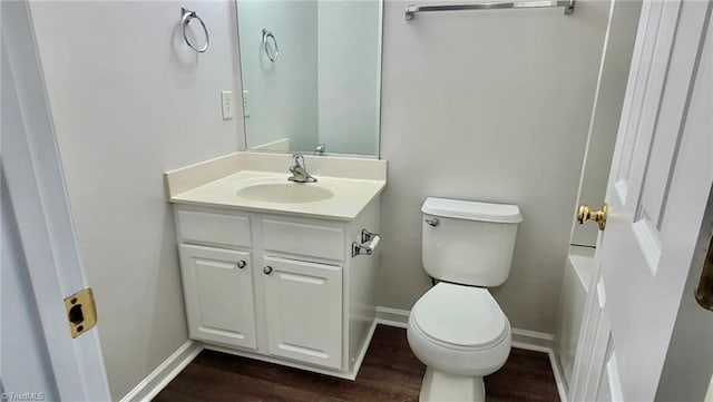 bathroom featuring baseboards, wood finished floors, toilet, and vanity