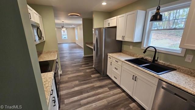 kitchen with plenty of natural light, stainless steel appliances, sink, white cabinetry, and hanging light fixtures