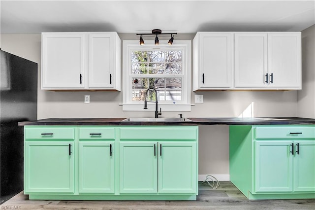 kitchen featuring black fridge, sink, white cabinets, and light hardwood / wood-style flooring