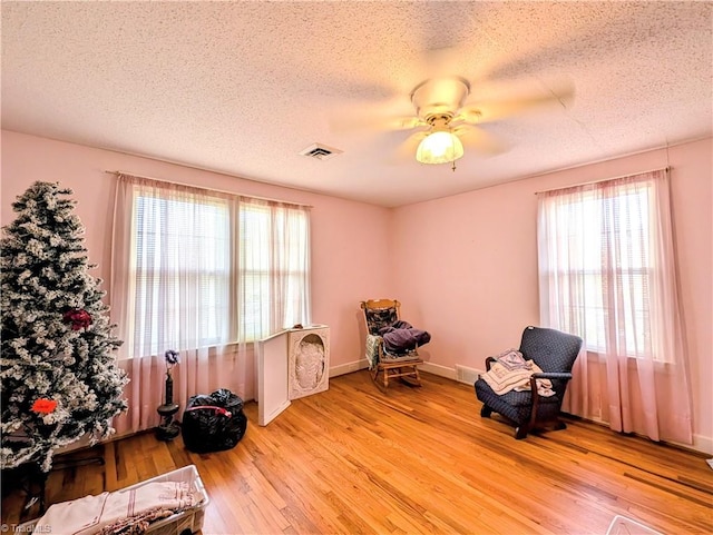 living area featuring a textured ceiling, light hardwood / wood-style floors, ceiling fan, and plenty of natural light