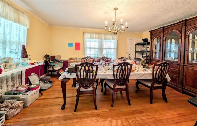 dining space featuring a textured ceiling, a notable chandelier, ornamental molding, and light hardwood / wood-style flooring