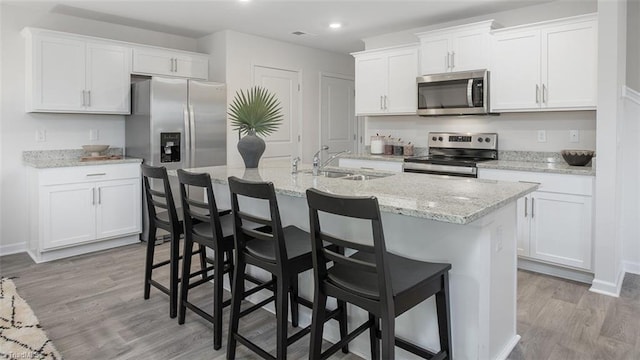 2124 Monk Dr, Haw River, NC 27258 - kitchen with appliances with stainless steel finishes, a sink, light wood-style flooring, white cabinets, and a kitchen breakfast bar